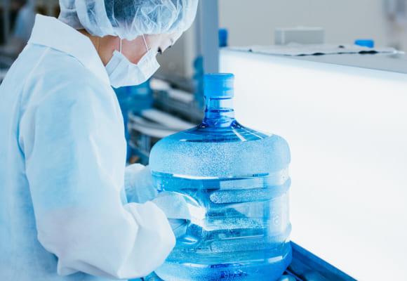 クリクラの工場で水の入ったボトルをチェックする女性