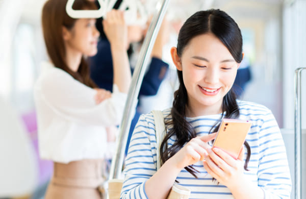 電車の中でスマートフォンを操作する女性の写真