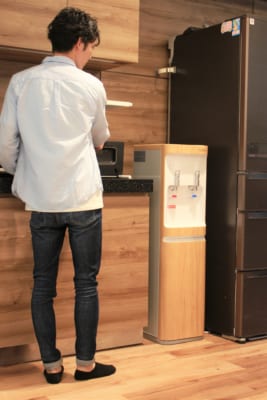 冷蔵庫とキッチンの間にコスモウォーターsmartプラスが設置されていて男性がウォーターサーバを見下ろしている様子